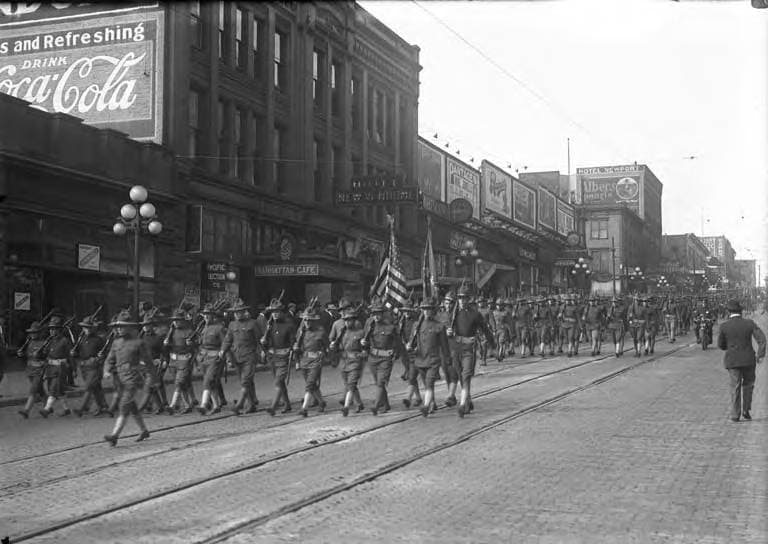 Black-and-white archival photograph of a World War I military column marching down 1st Avenue, Seattle, around 1917 to 1920, with the Hotel New Vendome sign visible mid-block