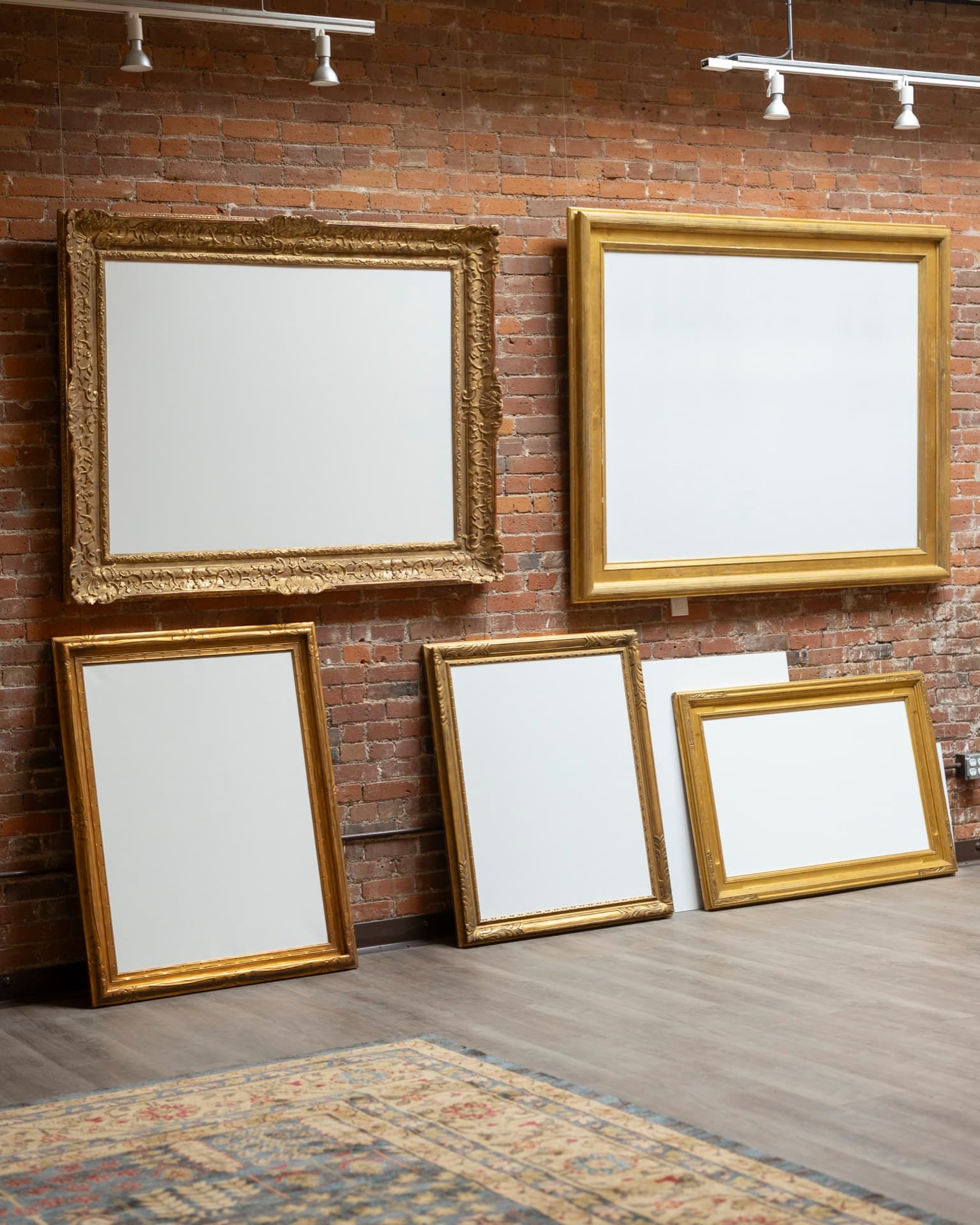 A grouping of gilt picture frames leaning against the exposed brick wall of the Occidental studios.